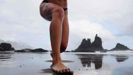 Una-Deportista-Hace-Ejercicios-A-Cámara-Lenta,-Estira-Las-Piernas-Y-Hace-Estocadas-En-La-Playa,-Mientras-Una-Mujer-Fitness-Practica-Ejercicios-Relajantes-Frente-Al-Mar