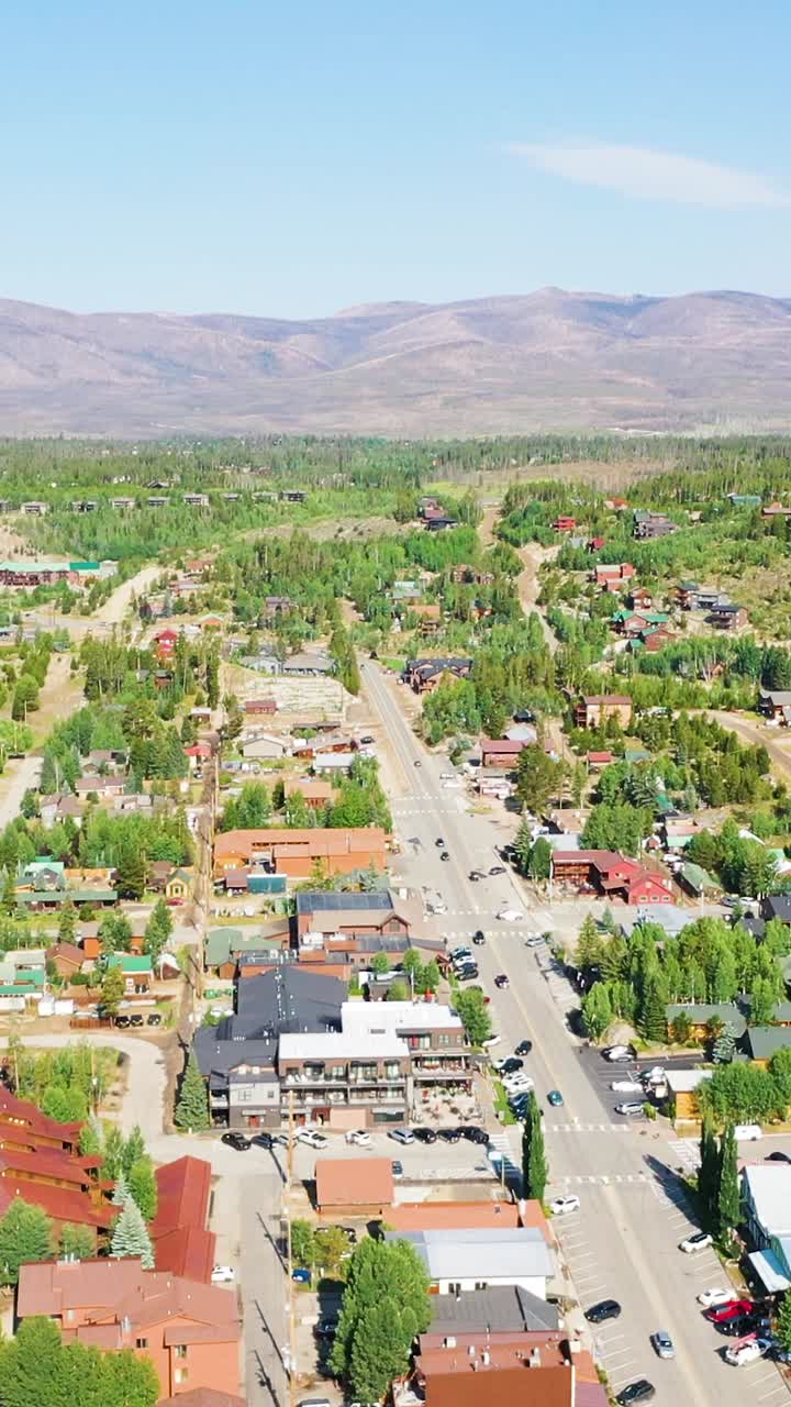 Vista aerea verticale dall'alto del Grand Lake Colorado con il quartiere del centro accanto al lago, incorniciato da pendii coperti di pini, creste montuose distanti e condizioni estive limpide