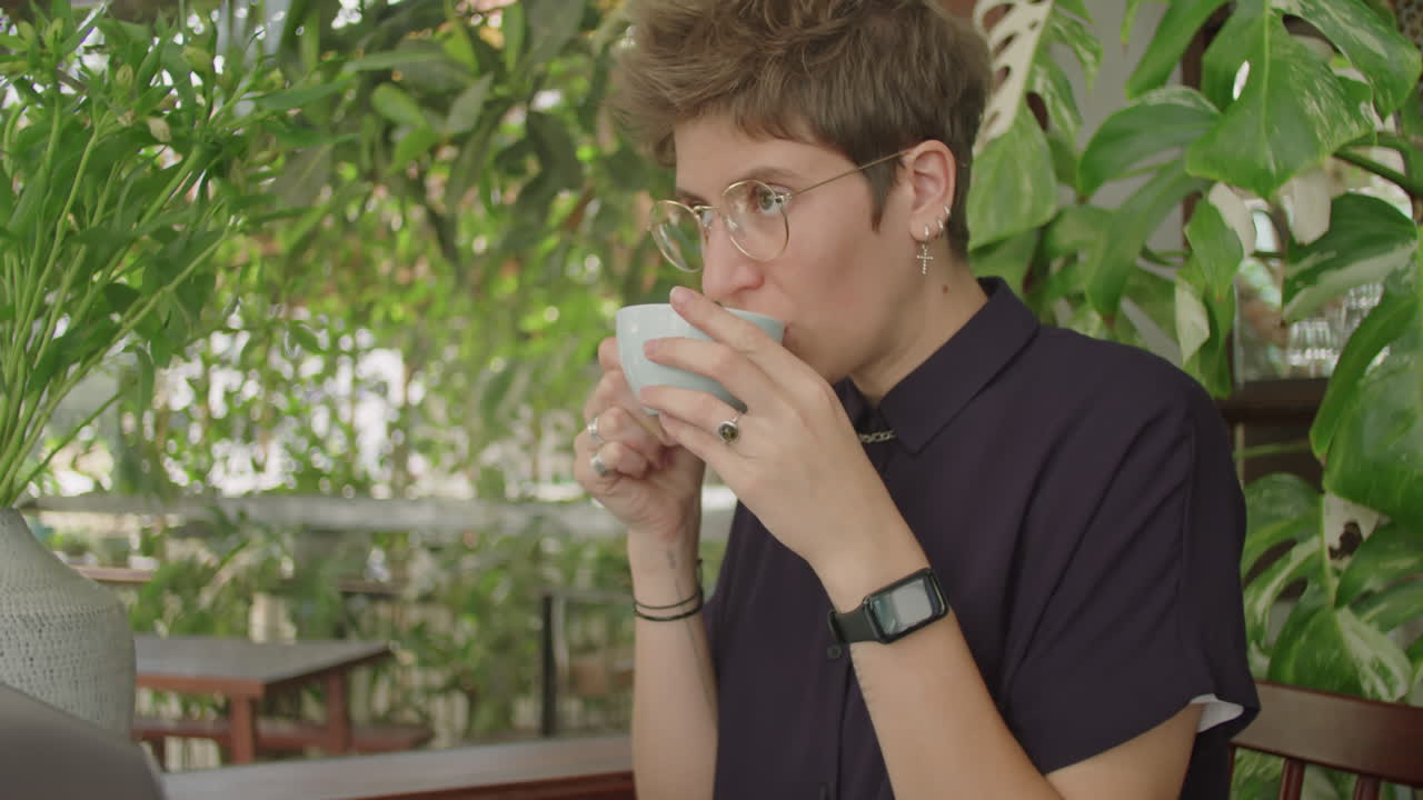 Woman Using Laptop and Drinking Coffee in Outdoor Cafe