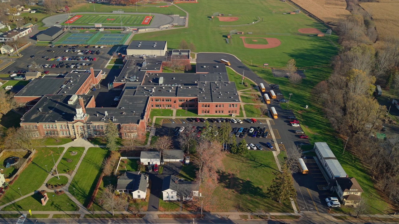 Flyfoto av et amerikansk skoleområde med idrettsbaner og skolebusser om høsten