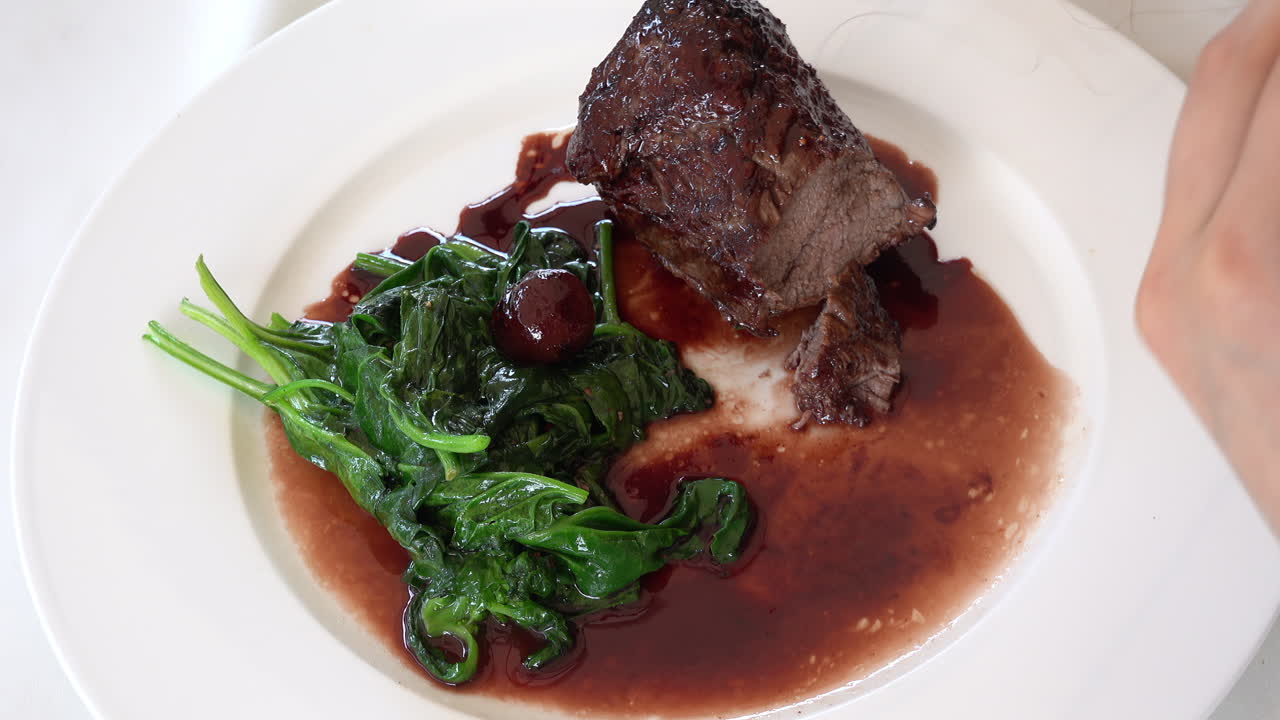 Woman cutting up a cooked beef tenderloin in sauce with greenery on a white plate