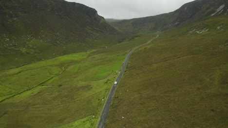 a small single white car makes its way through the amazing cinematic landscape of ireland