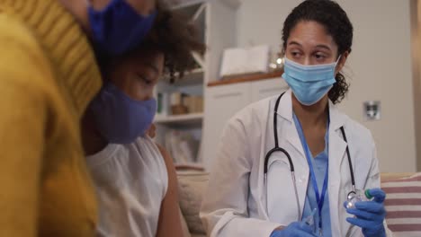 Mixed-race-female-doctor-wearing-face-mask-making-injection-at-home