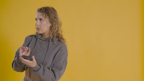 foto de estudio de una joven escuchando música en el teléfono móvil y bailando con fondo amarillo 2