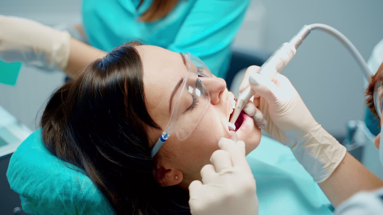 Woman patient with opened mouth at stomatology clinic. Professional dentist treating teeth using medical equipment. Close-up.