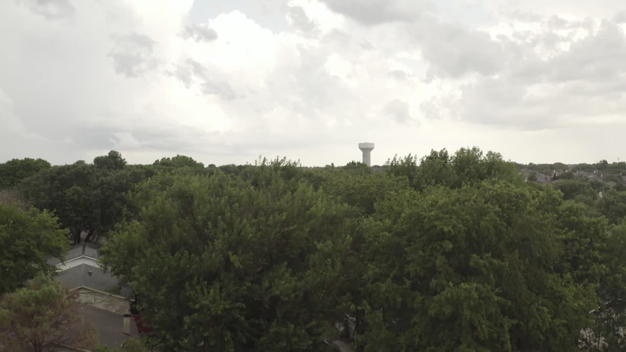 Pan down of a skyline with City water tank in the distance to the green treed neighborhood streets