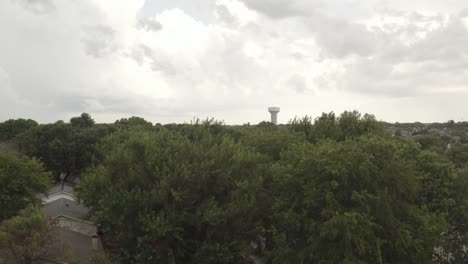 panorámica hacia abajo de un horizonte con tanque de agua de la ciudad en la distancia a las calles verdes del barrio arbolado