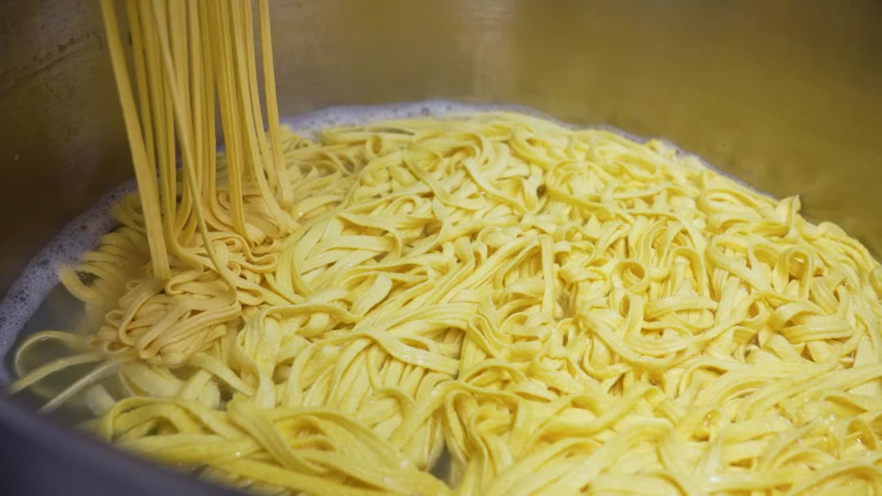 las hebras de fideos caseros frescos descienden lentamente en una gran olla de cocina