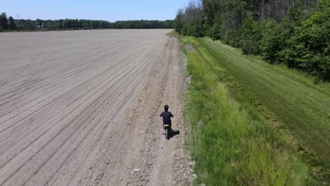 Drone-shot-following-a-young-man-riding-a-dirt-bike-on-a-farm