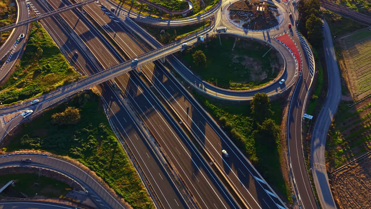 Traffic flows on a highway interchange with multiple lanes and roundabouts beside green fields during the late afternoon