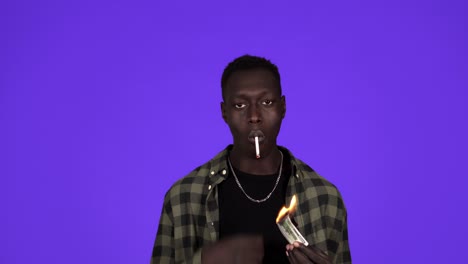 hombre serio con ropa casual y cadena de oro en el cuello está encendiendo su cigarrillo con billete de un dólar. concepto idea de riqueza, hombres ricos. aislado sobre fondo azul