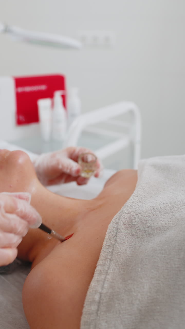 Cosmetologist applying special moisturizing acid serum peeling face chest of young woman in clinic