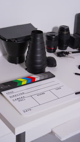 video vertical de primer plano de película clapperboard o pizarra con lentes de cámara y accesorios de iluminación rodando película o video en estudio