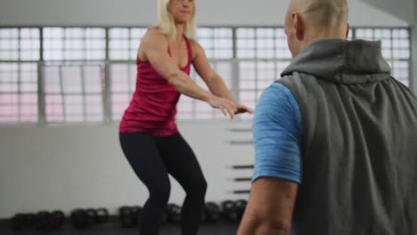 fit caucasian woman jumping on pylo box with male trainer at the gym