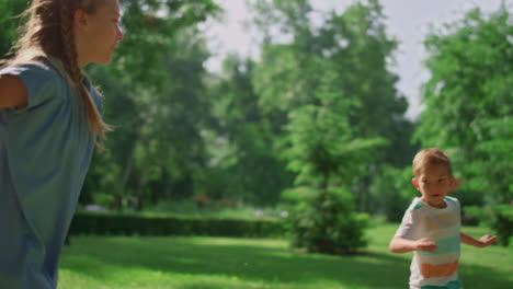 Pretty-sister-overtake-brother-on-lawn.-Happy-family-playing-catch-up-on-meadow.