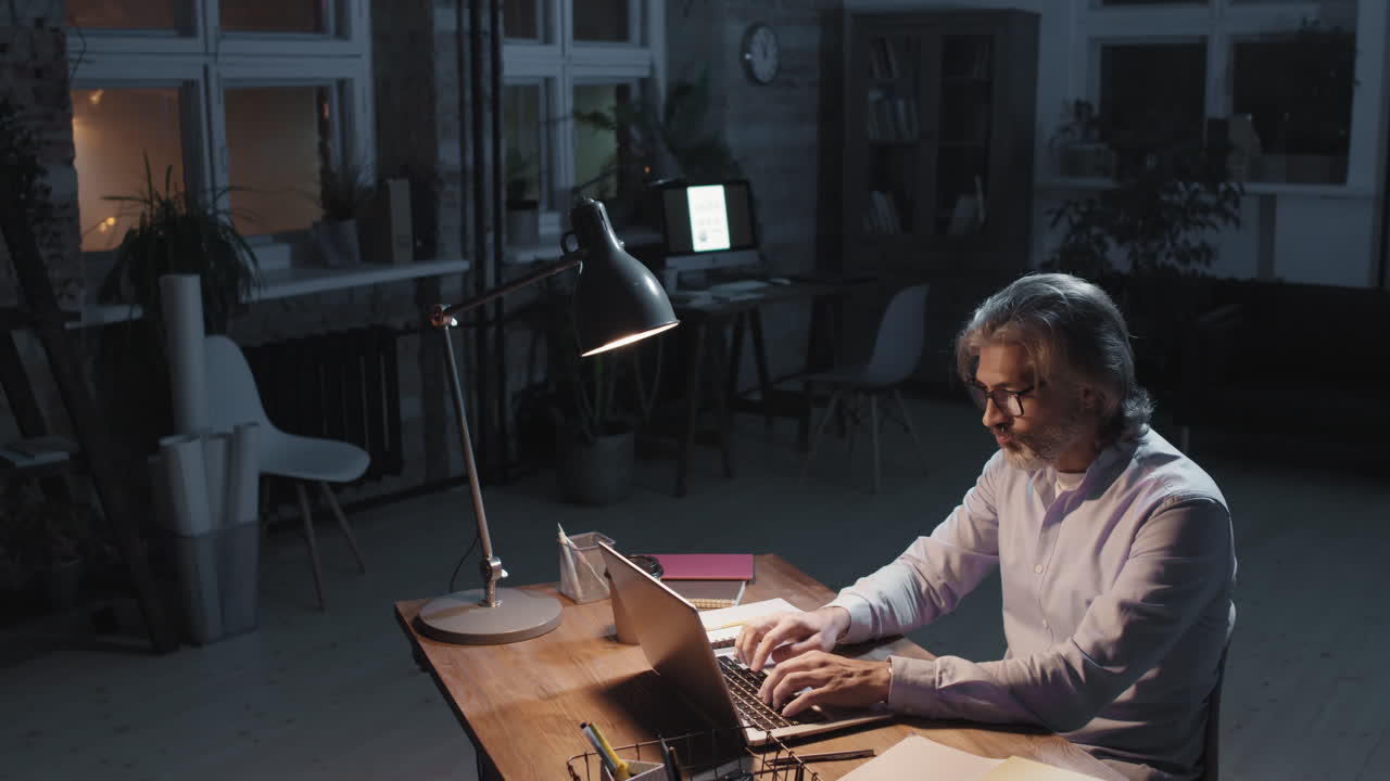 Man Working Late at Night on Laptop in Dimly Lit Office