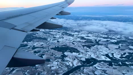 view from airplane window flying through snowy european landscape at dusk