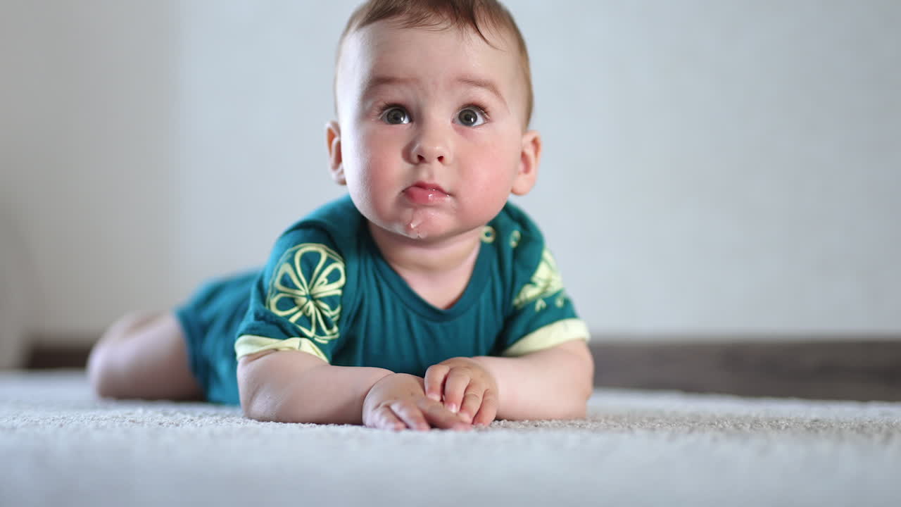 Cute active kid clapping hands by the floor. Baby lies on the carpet and looks around with interest and curiosity.