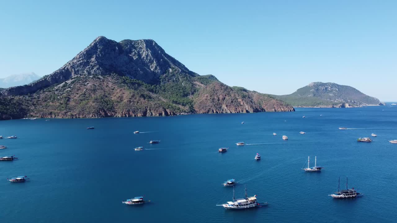 Aerial drone view showing mountainous coastline with leisure boats near Kas Antalya, capturing deep blue water, rugged slopes, bright summer light, calm sea surface, and wide coastal atmosphere