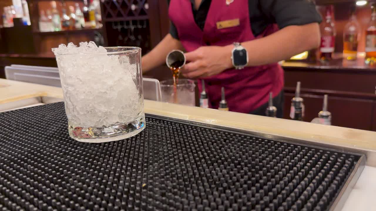 Bartender adds crushed ice and stirs cocktail in upscale bar with warm ambient lighting
