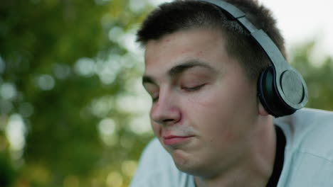 close up of man wearing headphones nodding his head to music while deeply focused, showcasing a serene and introspective expression, surrounded by blurred natural greenery in soft light