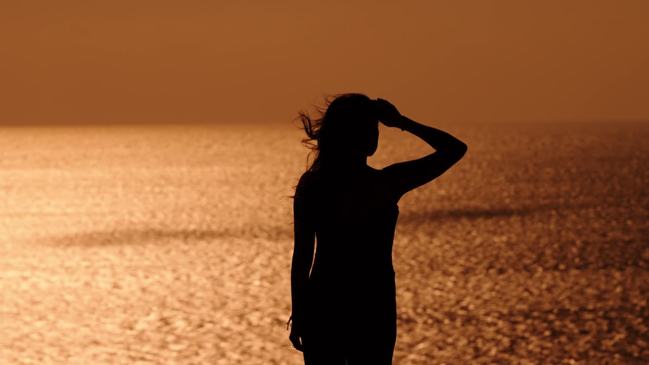 Silhouette of a woman gazing over the golden sea at sunset along Portugal's coast, evoking calm and reflection