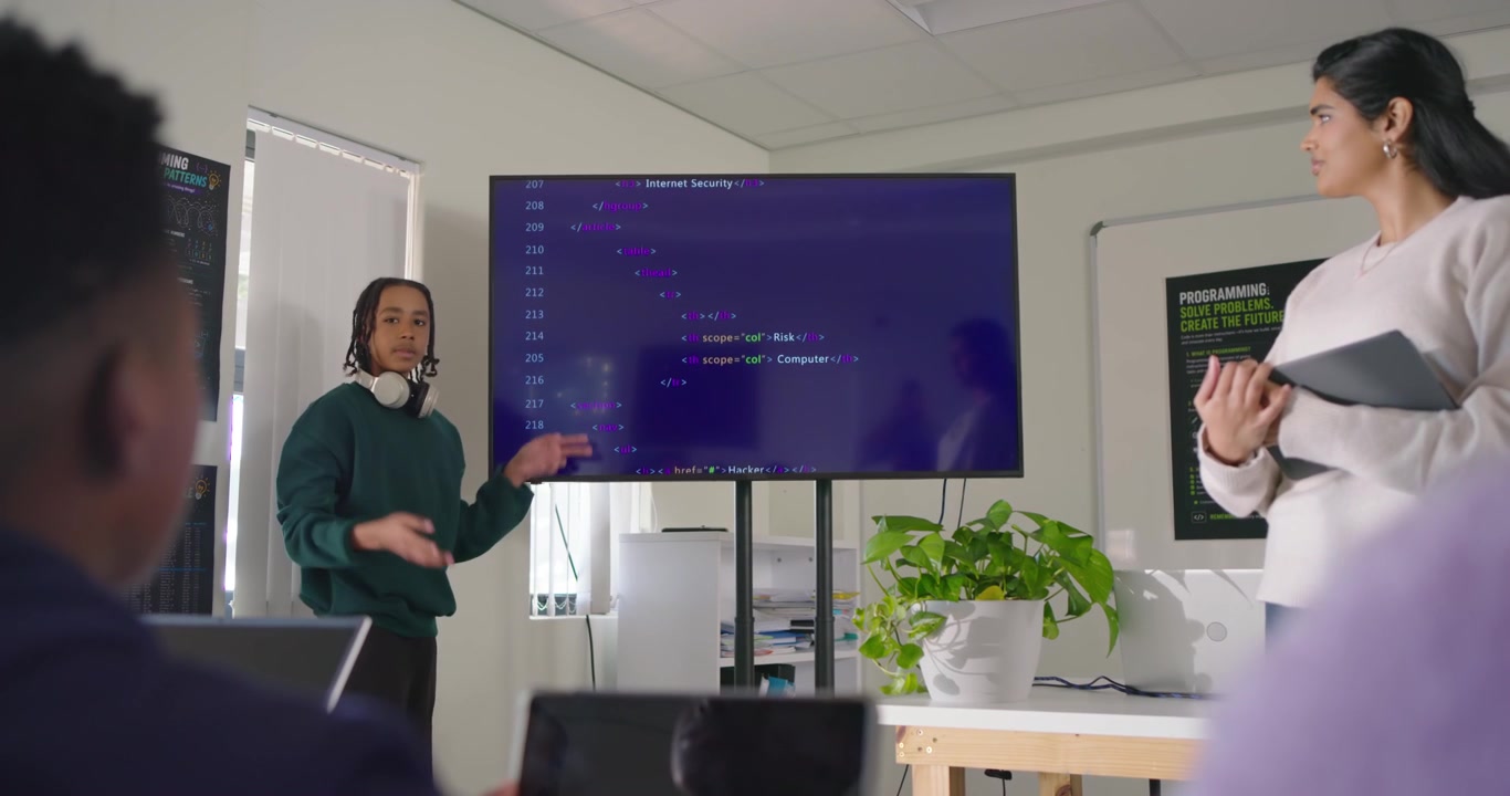 Teen African American presenting in lab pointing at code wearing headphones after teacher cue
