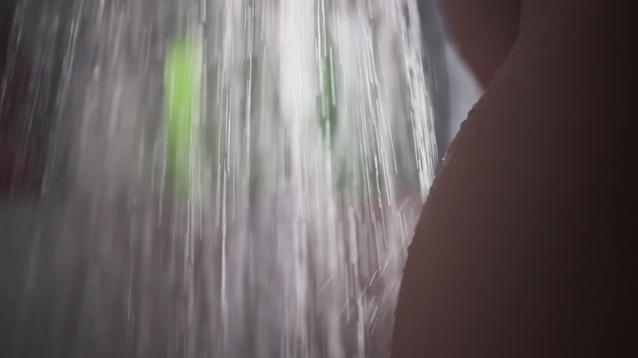강한 물의 흐름 아래에서 여성의 벌거벗은 몸. 여성은 욕실에서 뜨거운 물 아래에서 몸을 는다. 따뜻한 물 흐름 아래의 여성의 허지와 이.