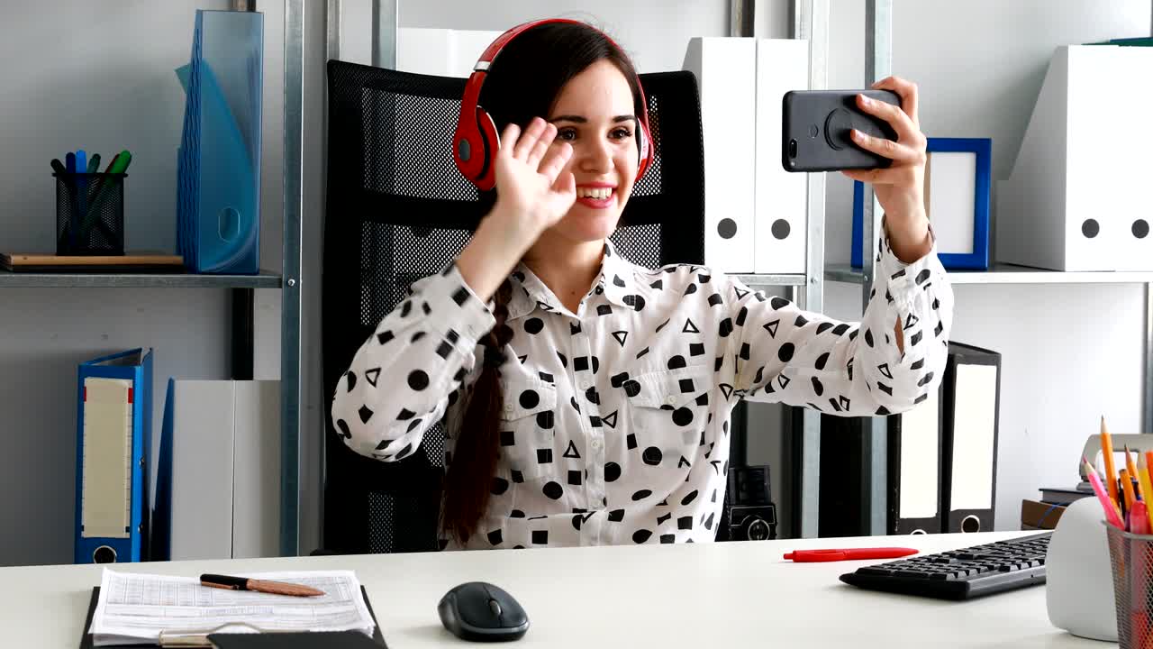 mujer de negocios con auriculares rojos grabando video en un teléfono inteligente en una oficina moderna