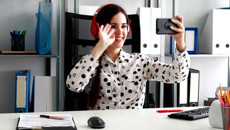 mujer de negocios con auriculares rojos grabando video en un teléfono inteligente en una oficina moderna