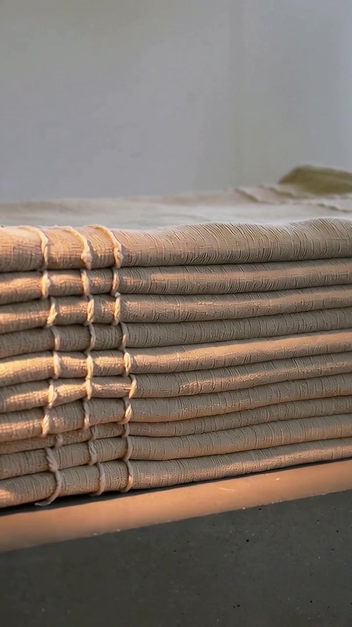 Video verticale: Luce che illumina biancheria color sabbia impilata con cuciture a vista su una scrivania scura da studio
