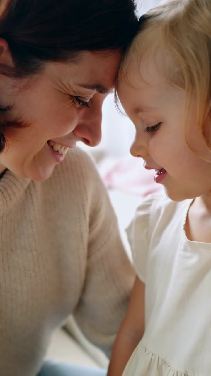 Vertikales Video: Kinderstimme zu hören, Mutter und Kind drücken zu Hause Stirnen aneinander, Strickpullover