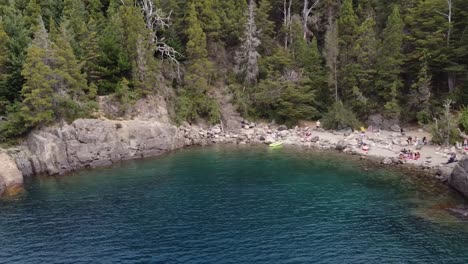 Aerial-dolly-shot-of-tourist-relaxing-on-a-rocky-beach-in-a-lake-surrounded-by-forest-in-Patagonia-Argentina