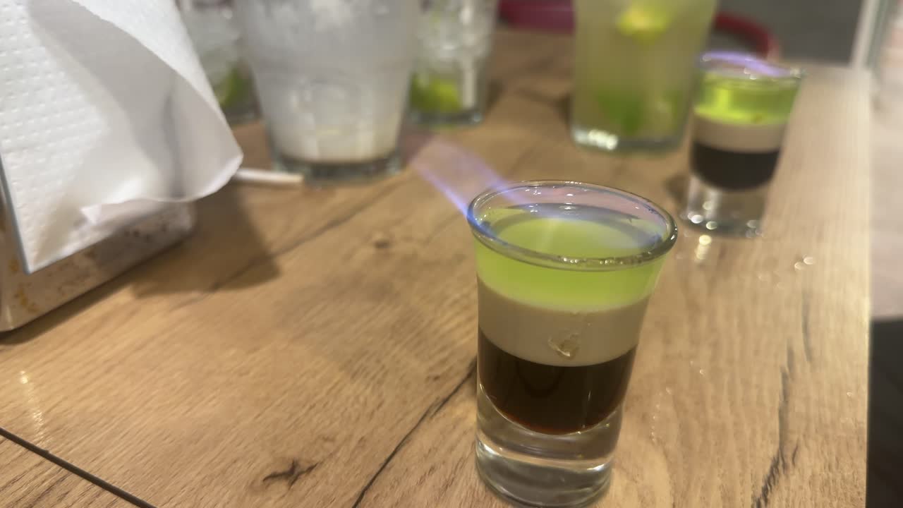İç mekanda, ahşap bir masada shot bardağında küçük katmanlı bir içecek.