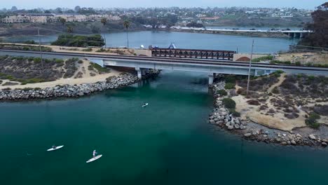 Paddle-Boarders-En-La-Laguna-De-Carlsbad,-Vista-De-Drones-Al-Mirar-I-5-Norte,-I-5-Sur