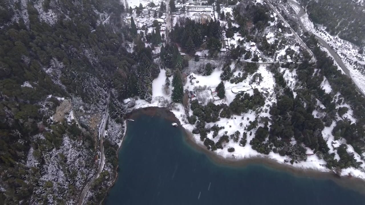Ripresa aerea con drone sopra la costa innevata e la foresta a Colonia Suiza, Río Negro, Argentina, scatto dall'alto di un paesaggio invernale vicino al Lago Nahuel Huapi durante una nevicata.