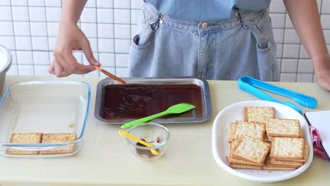 a woman's hand soaks the biscuits in coffee and places them on a glass bowl to make a tiramisu cake