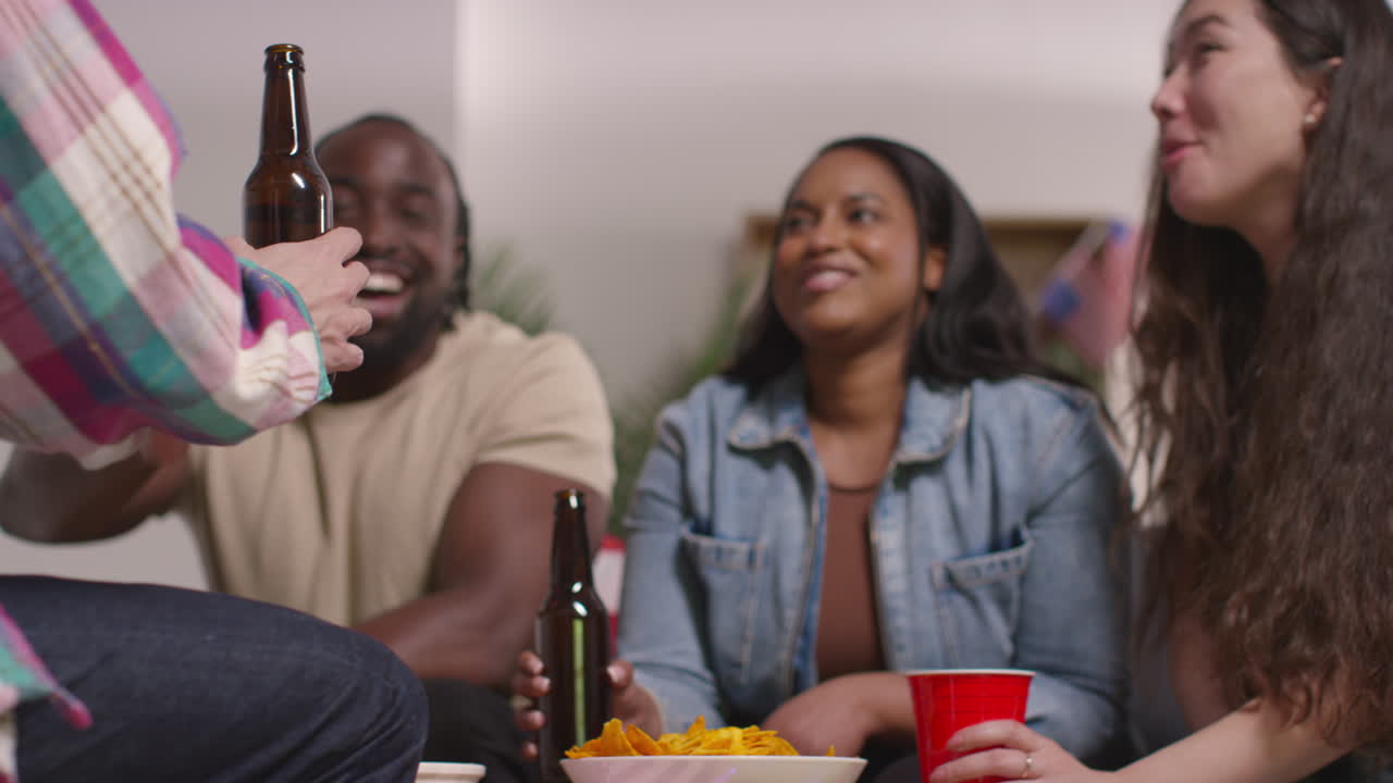 Friends At Home Laughing Talking And Eating Snacks Celebrating At Party Doing Cheers With Alcohol