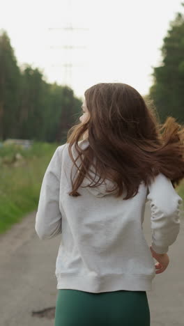 mujer con el cabello suelto corre a lo largo de la carretera cerca de los arbustos del bosque. atleta en uniforme deportivo mira a su alrededor corriendo más allá de los árboles en la acera. mejorar la forma del cuerpo y la salud física