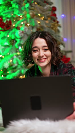 positive happy brunette girl opens her laptop. portrait of woman starting work from home near the christmas tree. vertical video.