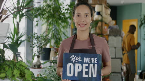 Smiling Woman in a Plant Shop Holds an Open Sign