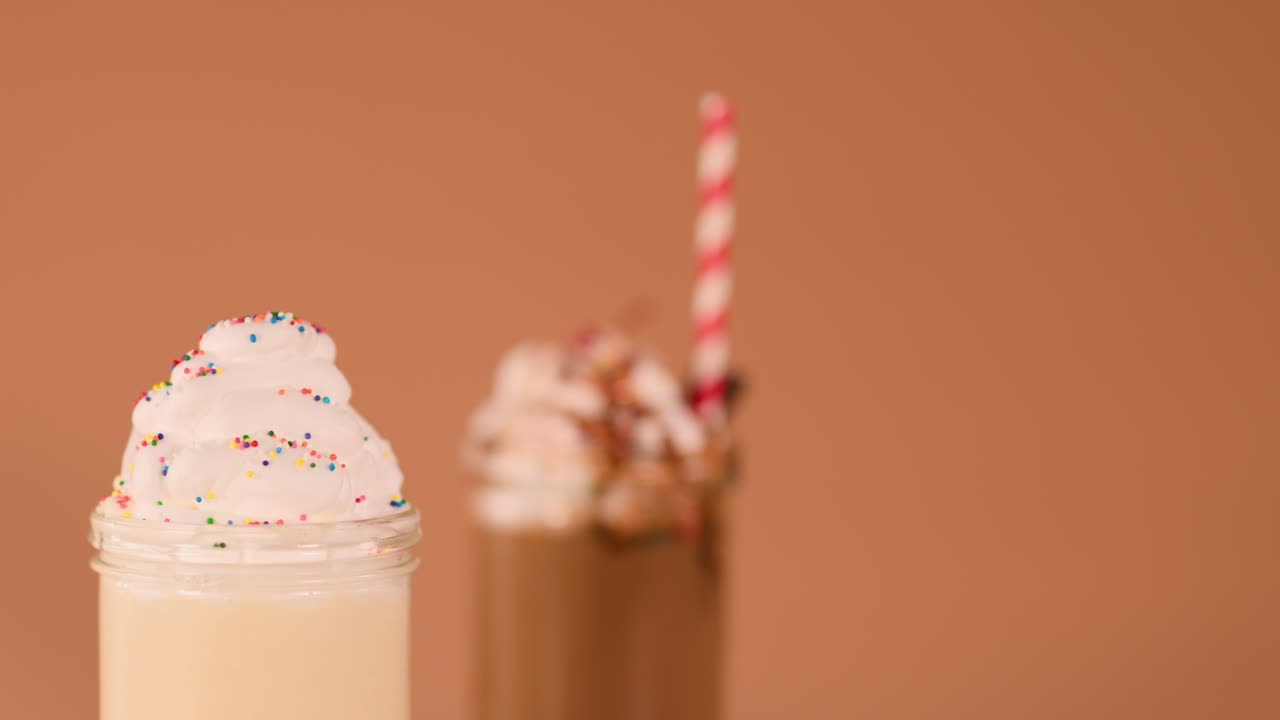 Close-up of hand topping vanilla milkshake with cherry, colorful sprinkles, and soft studio lighting