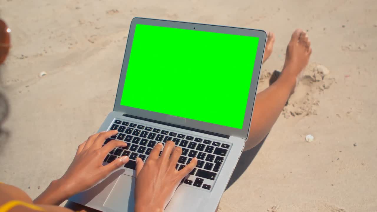 Young woman sitting and using laptop on beach in the sunshine 4k