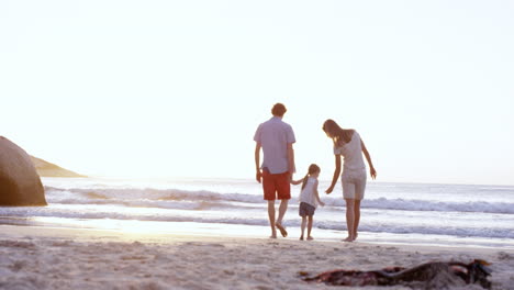 Familia-Feliz-Jugando-En-La-Playa-Caminando-Hacia-El-Océano-Tomados-De-La-Mano-Al-Atardecer-De-Vacaciones