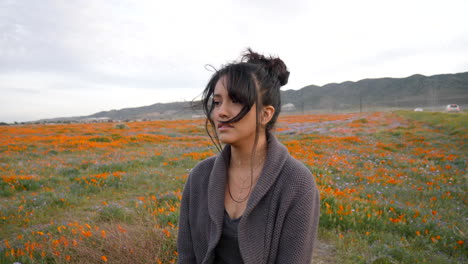 a beautiful young woman crying and looking emotional and sad in a field of wild flowers with wind blowing her hair at sunset in slow motion