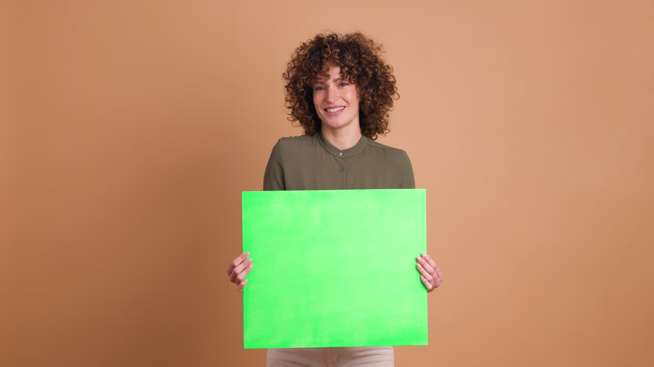 Happy woman holding blank green paper in beige studio