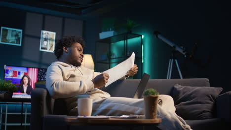 young black person overseeing schedule and planning activities at his home, working on time management with online tools. male adult utilizing a calendar on pc and checking the planner. camera b.