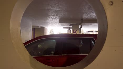 View-of-driver's-side-of-red-SUV-looking-through-a-concrete-portal-in-a-mall-parking-garage-in-winter