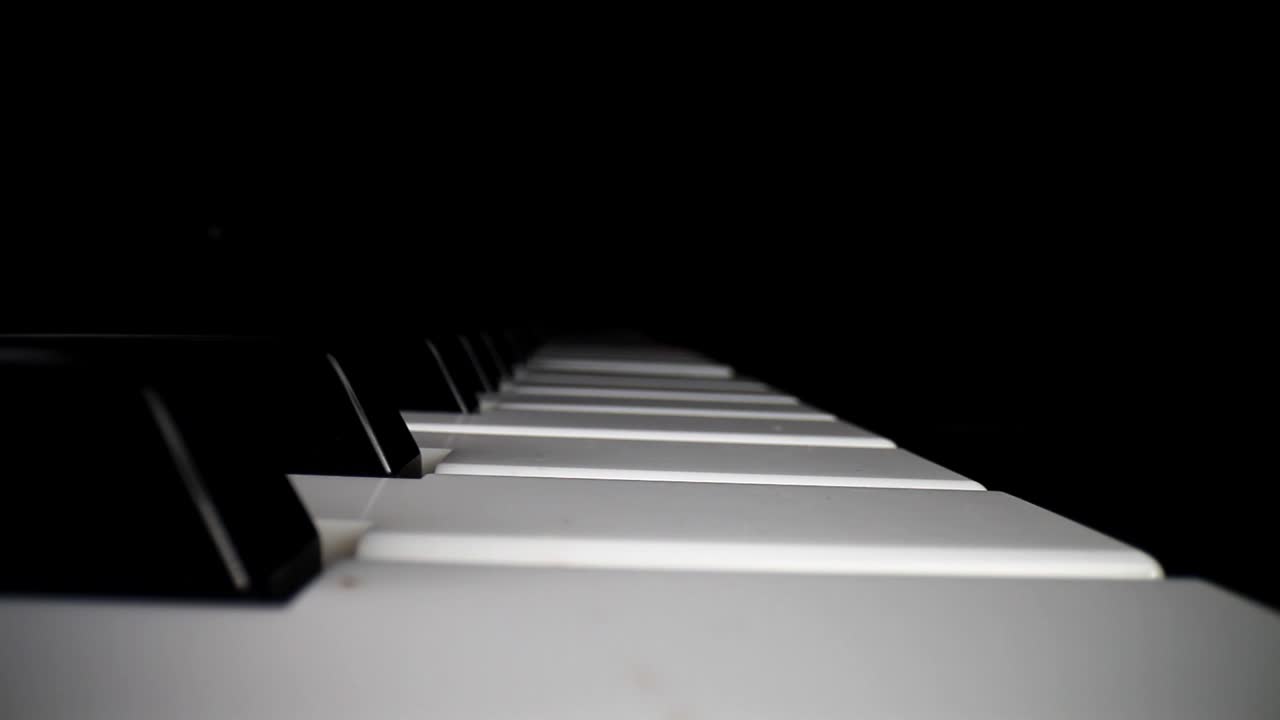 Wide angle macro of electronic keyboard - static shot of keyboard and the song assist lighting the keys a red color, movement down and then pulling away from keys as song continues to play