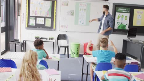 Diverse-male-teacher-and-happy-schoolchildren-at-desk-in-school-classroom